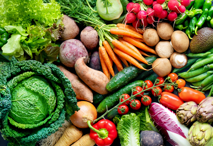 Eine Vielzahl von frischem Gemüse, darunter Kopfsalat, Radieschen, Karotten, Gurken, und Paprika, auf einem Tisch angeordnet.