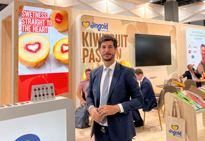 Federico Milanese steht in einem Messestand von Jingold. Im Hintergrund sind Kiwis und der Slogan 'SWEETNESS STRAIGHT TO THE HEART' zu sehen. Der Stand hat eine helle Holzoptik.