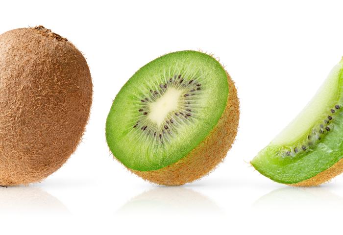 Eine ganze Kiwi links, in der Mitte eine halbierte Kiwi mit grünem Fruchtfleisch und schwarzen Kernen, rechts ein Viertel einer Kiwi mit grünem Fruchtfleisch.