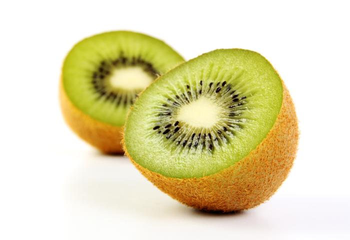 Zwei Hälften einer Kiwi mit grünem Fruchtfleisch und schwarzen Kernen, die auf einer weißen Fläche liegen.