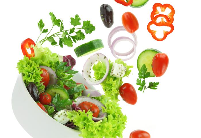 Eine weiße Schüssel mit gemischtem Salat, darunter grüne Blätter, Kirschtomaten, Gurkenscheiben, rote Paprika und Zwiebelringe, die in der Luft schweben.