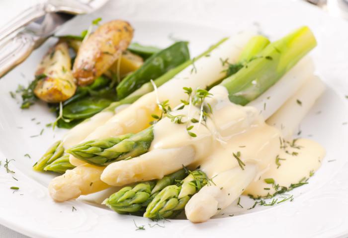 Ein Teller mit Spargel, grünem Gemüse und kleinen Kartoffeln. Der Spargel ist mit einer hellen Sauce und frischen Kräutern garniert.