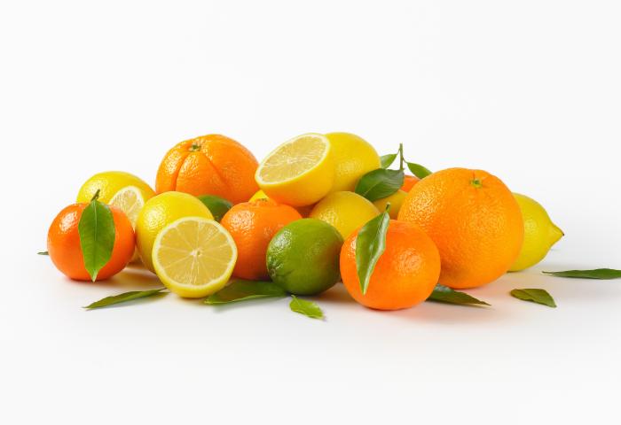 Eine Anordnung von Orangen, Zitronen und einer Limette mit grünen Blättern, einige Früchte sind halbiert und zeigen das Fruchtfleisch.