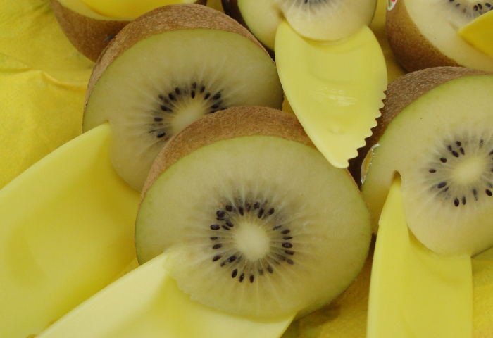 Zespri SunGold Kiwi, halbiert, mit gelben Löffeln zum Servieren. Die Frucht hat eine gelbliche Innenseite mit kleinen schwarzen Kernen.