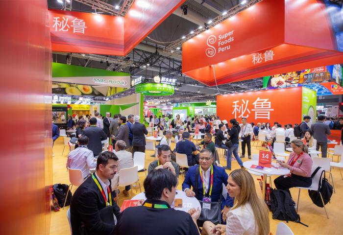 Messehalle mit vielen Personen an Tischen, rotes Banner mit 'Super Foods Peru' und chinesischen Schriftzeichen, lebhafte Atmosphäre.
