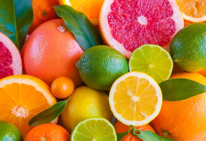 Eine Vielzahl von Citrusfrüchten, darunter Grapefruits, Orangen, Zitronen, Limetten und Mandarinen, liegen übereinander. Einige Früchte sind halbiert, um das Fruchtfleisch zu zeigen.