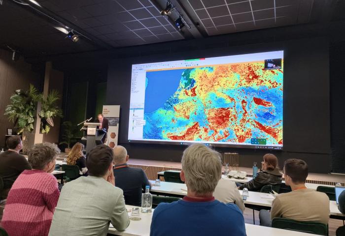 Tomislav Hengl präsentiert farbige Datenvisualisierungen des Soil Health Data Cube auf einer großen Leinwand. Im Vordergrund sind Zuhörer in einem Konferenzraum zu sehen.