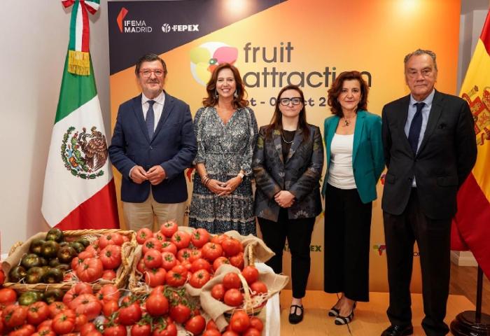 Fünf Personen stehen vor einer Wand mit dem Text 'fruit attraction' und den Flaggen von Mexiko und Spanien. Vor ihnen liegen Körbe mit Tomaten auf einer Präsentationsfläche