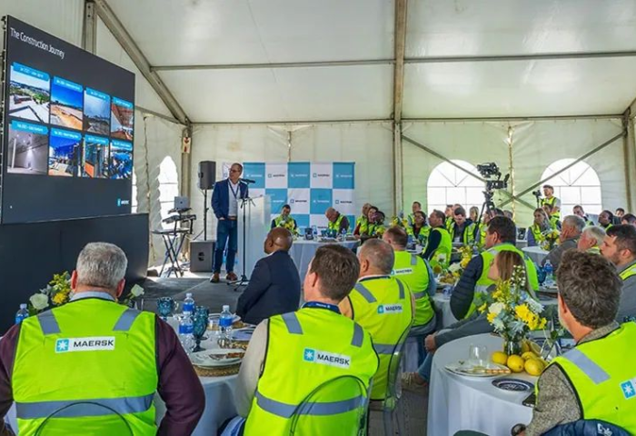 Eine Präsentation in einem Zelt mit einem Redner vor einer Leinwand. Die Zuhörer tragen gelbe Maersk-Sicherheitswesten. 