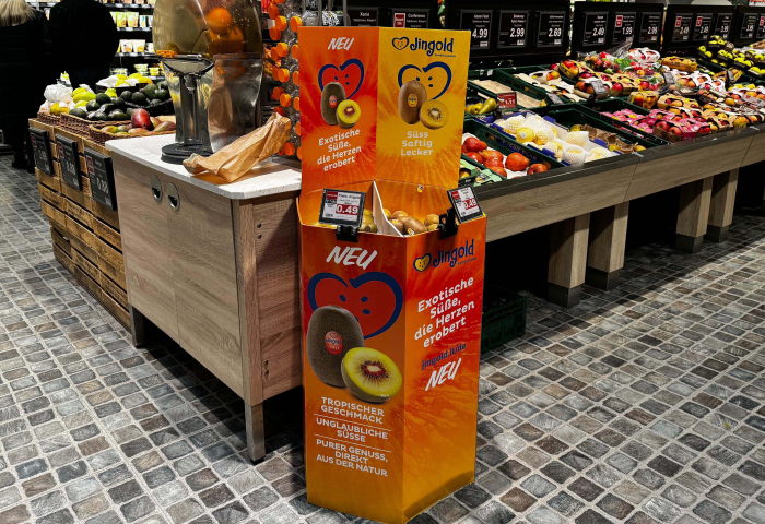 Ein Verkaufsstand von Jingold mit einer Auswahl an Kiwis. Der Stand zeigt die Aufschrift 'NEU' und Informationen zu tropischen Früchten. Im Hintergrund sind Obst- und Gemüseregale sichtbar.