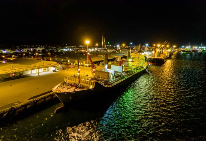 Großes Frachtschiff mit Containern im Hafen bei Nacht. Beleuchtete Hafenanlagen im Hintergrund.