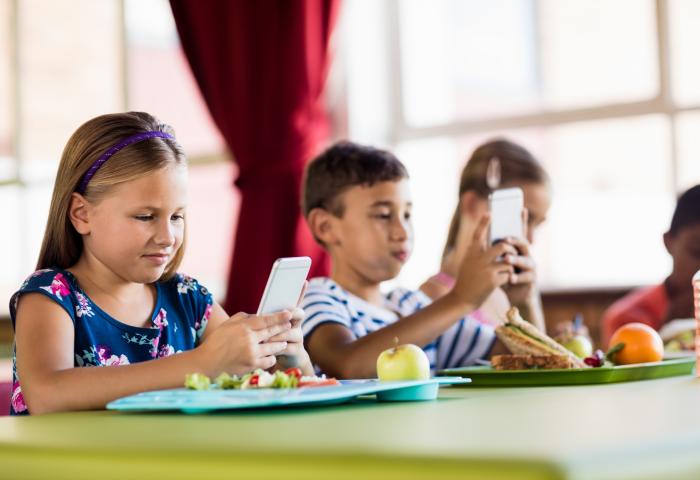 Kinder mit Smartphone und Essen in der Schule
