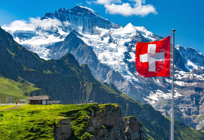 Schweizer Fahne weht vor einem schneebedeckten Berg und einer Hütte