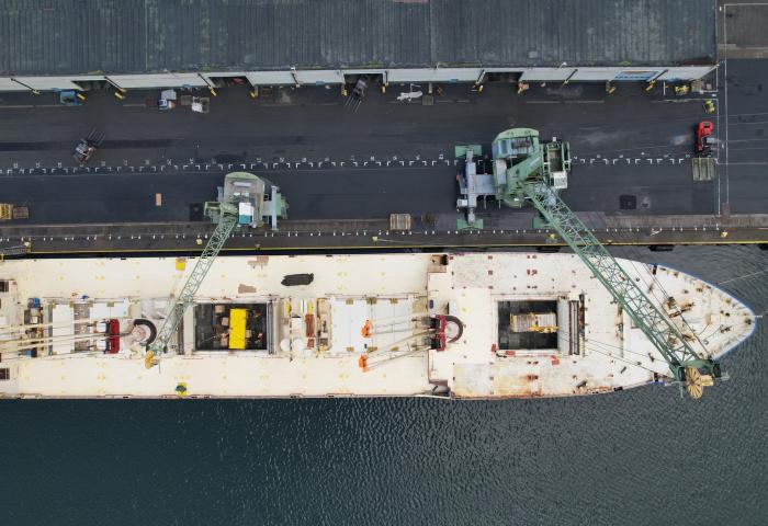 Luftaufnahme eines beladenen Frachtschiffs am Hafen mit Kränen und Lagerbereich am Kai