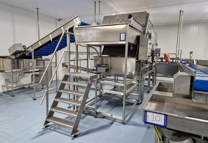 Große Edelstahlmaschine mit Treppe, Förderbändern und mehreren nummerierten Stationen in einer Produktionshalle.