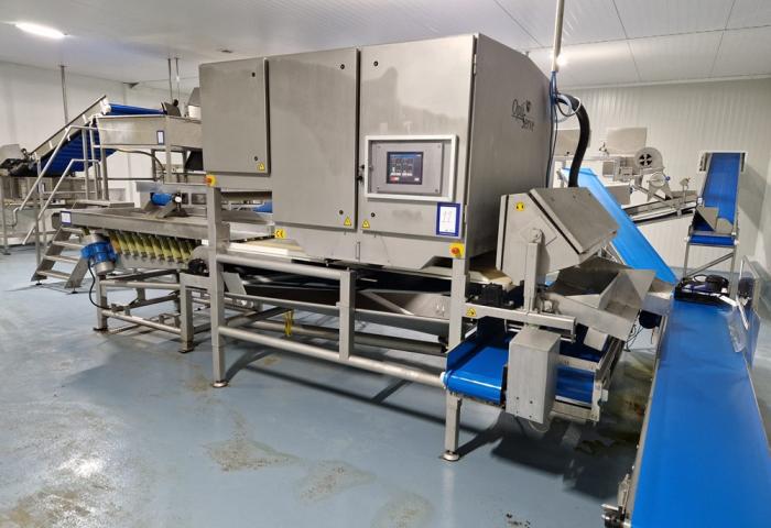 Große industrielle Maschine mit mehreren Förderbändern und Steuerungstafel in einer Produktionshalle mit grauem Boden.