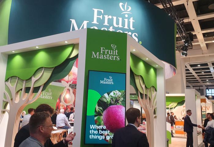 Messestand von Fruit Masters mit grün-weißer Gestaltung, Baum-Dekorationen und digitalem Bildschirm mit Text 'Where the best things grow'.