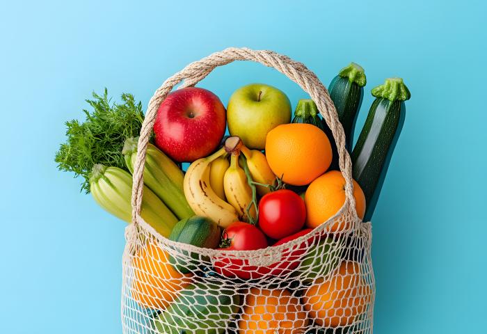 Eine Einkaufstasche mit Obst und Gemüse vor blauem Hintergrund.