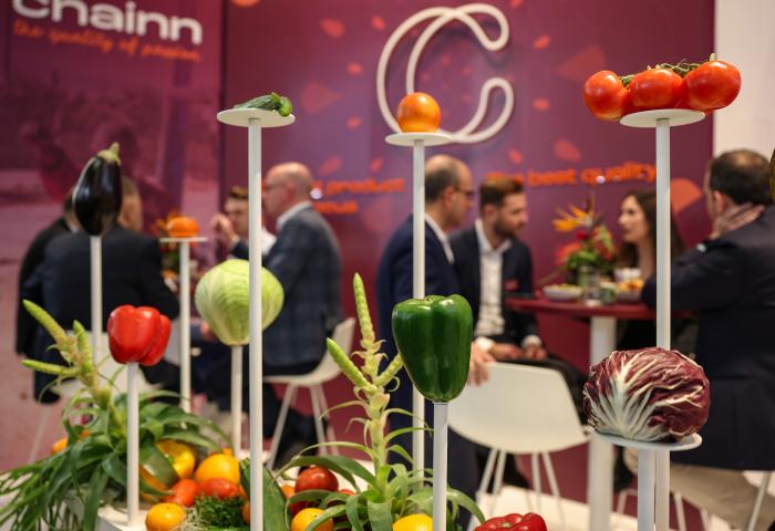 Intensive Gespräche auf der Fruit Logistica in Berlin. Im Vordergrund sind verschiedene Gemüsesorten zu sehen. 
