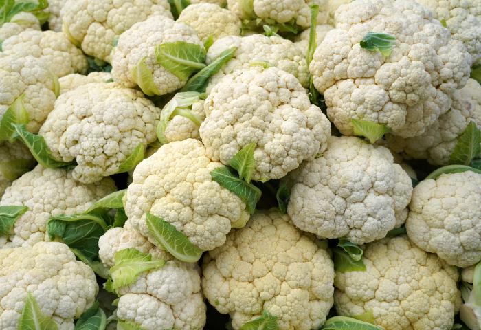 Mehrere frische Blumenkohlköpfe mit grünen Blättern liegen dicht beieinander.