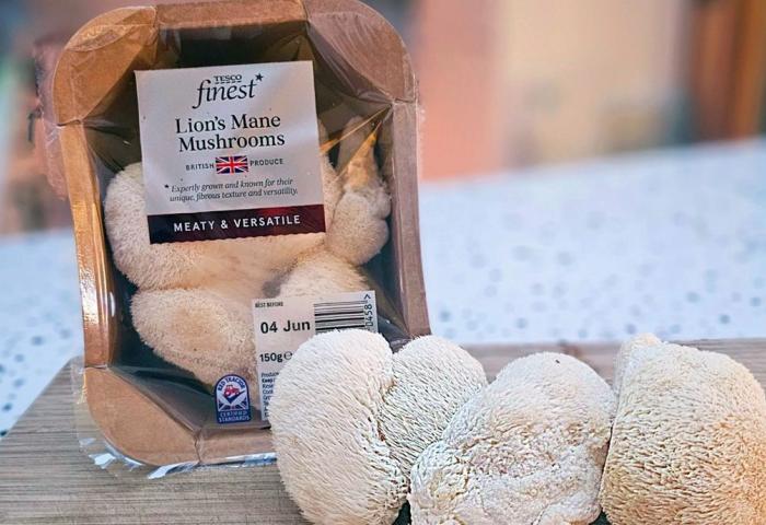 Verpackung mit sichtbaren Löwenmähne Pilzen darin, drei weitere Pilze lose davor