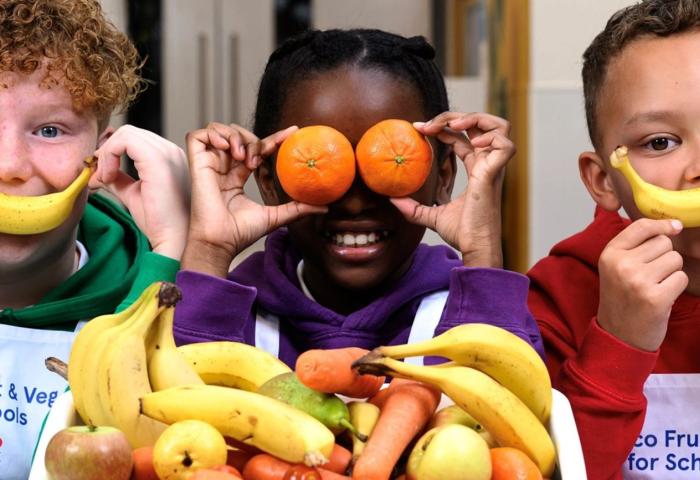 Kinder halten sich Bananen und Mandarinen vor Augen und Mund