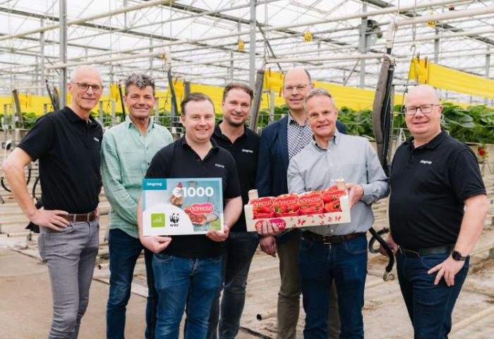 Gruppe von sieben Personen in Gewächshaus, einer hält eine Geschenkkarte und ein weiterer eine Kiste mit Erdbeeren.
