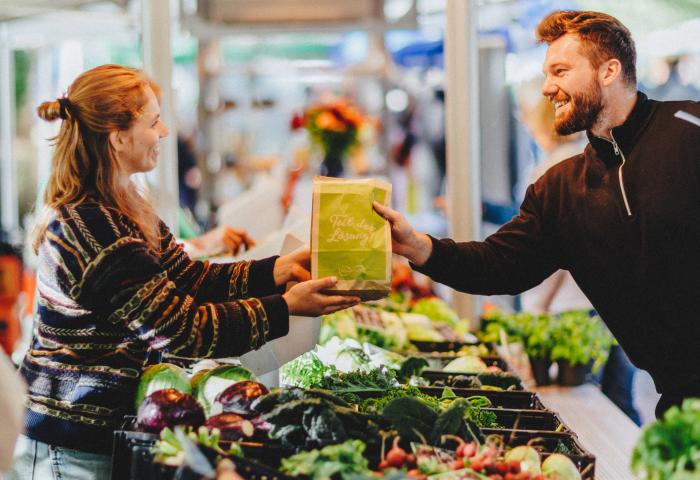 Marktstand an dem ein Mann einer Frau einen Beutel mit Bio-Lebensmittel gibt