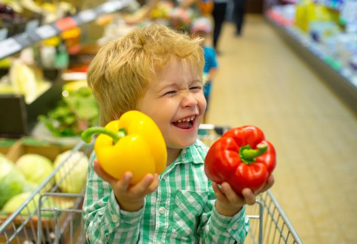 Junge lacht und hält rote und gelbe Paprika in der Hand