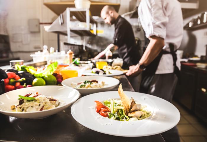 Eine Küche im Gastgewerbe. Im Vordergrund stehen Teller mit zubereiteten Speisen.