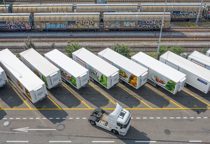 Weiße Kühlcontailer für Obst und Gemüse von Migros warten auf den Abtransport durch Lkw.