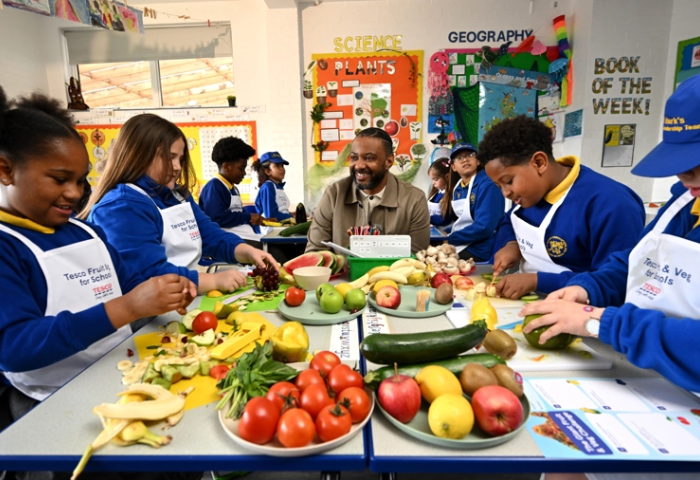 Britische Schulkinder sitzen gemeinsam an einem Tisch und schneiden Obst und Gemüse.