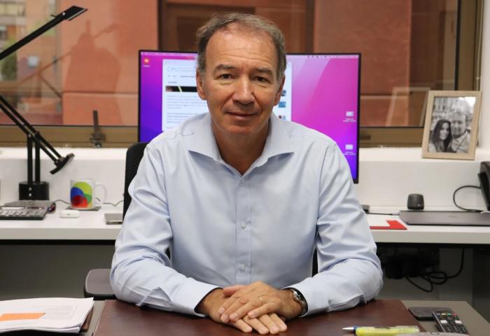Mann sitzt an Schreibtisch mit Computer im Hintergrund