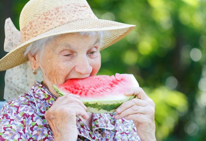 ältere Frau mit Hut beißt in ein Stück Wassermelone
