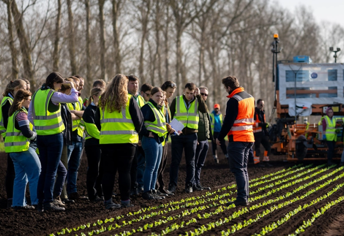 Junge britische Landwirte stehen in hellen Sicherheitswesten vor einem Feld.
