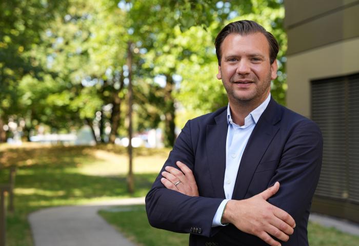 Mann mit verschränkten Armen in blauer Jacke und weißem Hemd.