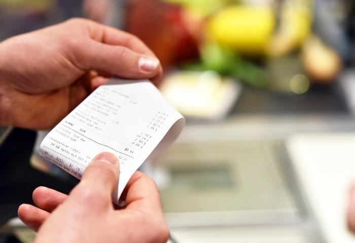 Eine Person hält einen ausgedruckten Kassenbon an einer Supermarktkasse in den Händen.