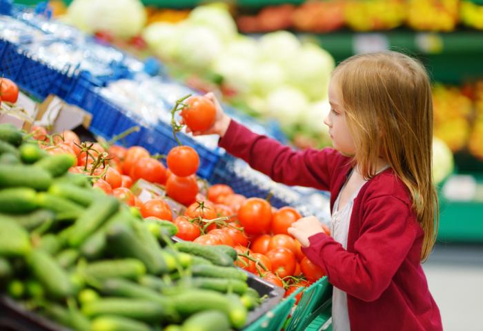 Kind greift nach Tomaten im Regal