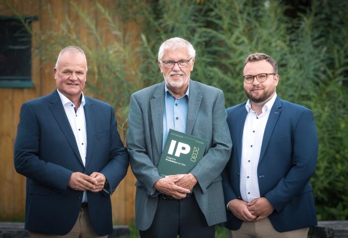 Drei Männer stehen nebeneinander, der in der Mitte hat einen Ordner, auf dem IP steht.