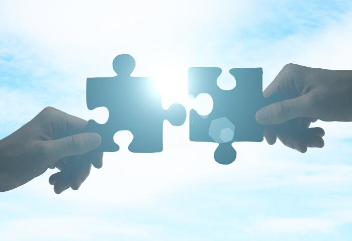 zwei Hände stecken zwei Puzzleteile zusammen