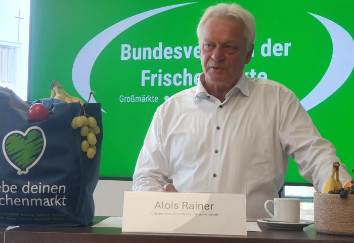 Mann steht an Tisch mit Tasche neben sich, die mit Obst und Gemüse gefüllt is