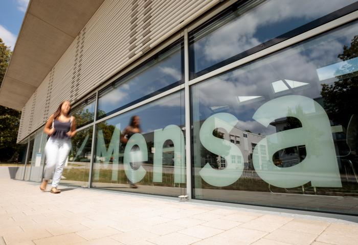 Person läuft vor Gebäude mit Mensa-Schriftzug vorbei