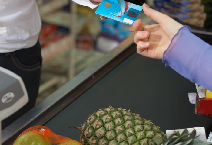 Person reicht Girokarte über Kasse zum Bezahlen