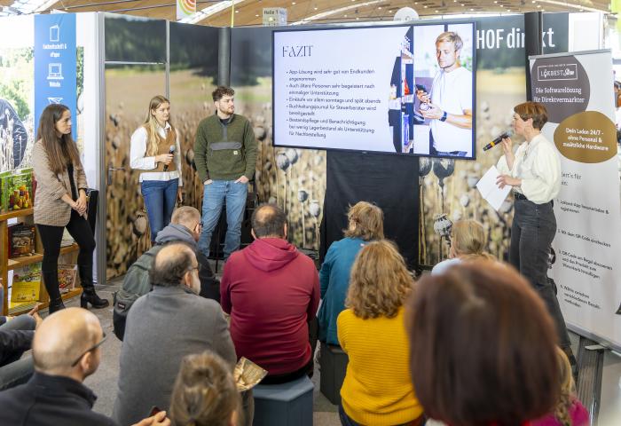 Referenten stehen neben Infoscreen vor Plenum
