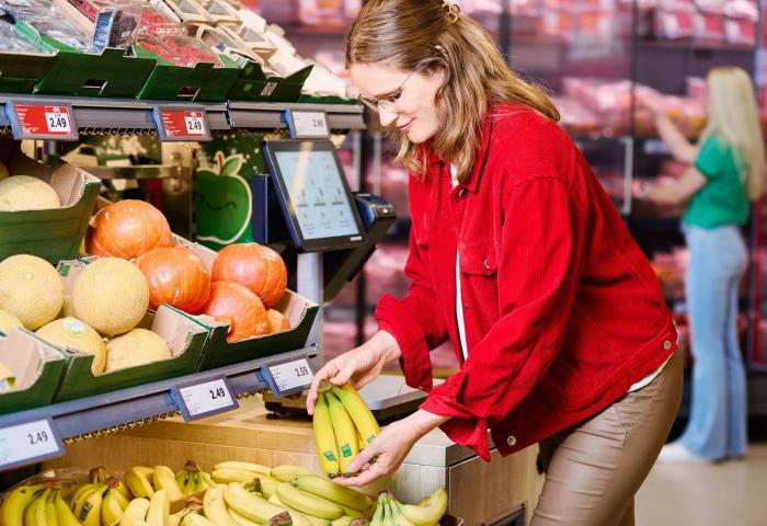 Frau steht vor Obstregal und hält Bananen in der Hand