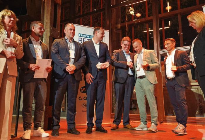 Männer und Frauen stehen mit Trophäe in der Hand auf der Bühne