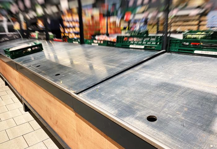 Weitgehend leere Auslage in der Obst- und Gemüseabteilung eines Supermarkts, mit wenigen grünen Warenkisten im Hintergrund.