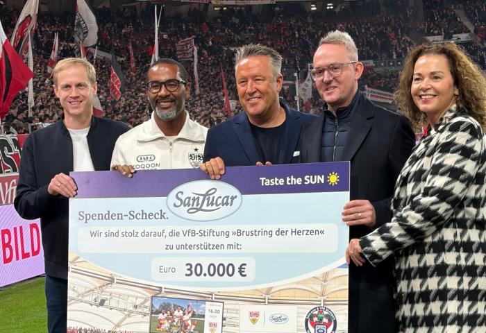 Menschen stehen mit symbolischem Scheck auf Rasen