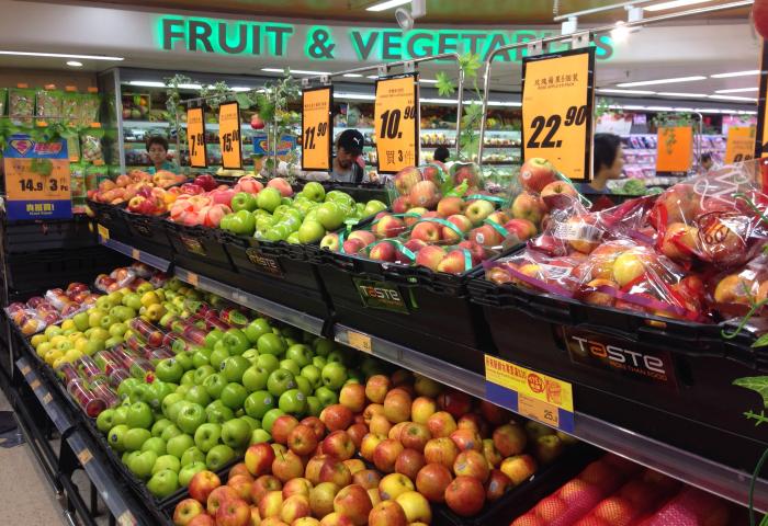 Obstauslage in einem Supermarkt in Hongkong mit roten und grünen Äpfeln, lose und verpackt, sowie darüber angebrachten Preisschildern.