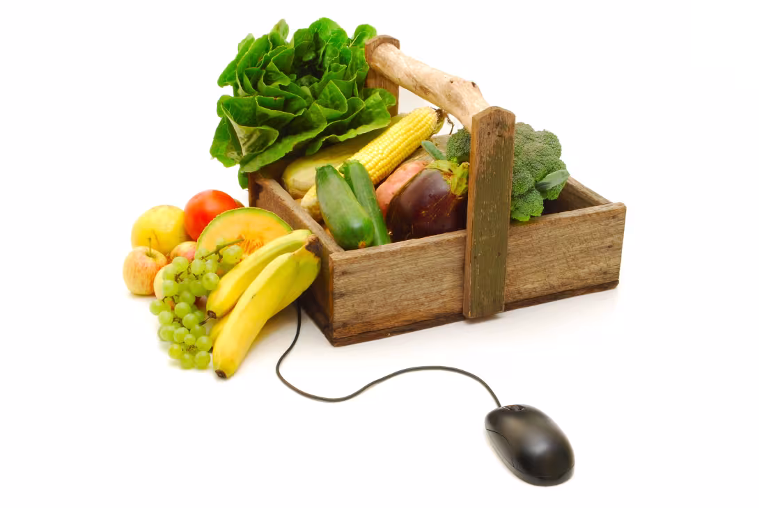 Holzkiste mit Salat, Mais, Brokkoli, Zucchini, Aubergine, Bananen, Trauben und Äpfeln, verbunden mit einer Computermaus
